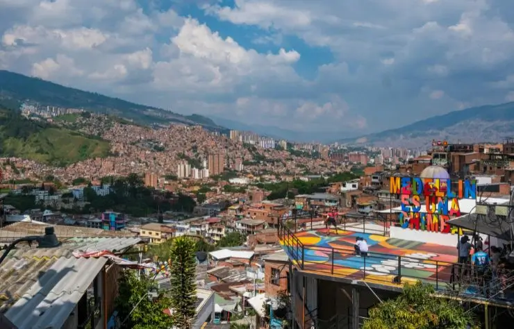 Medellin Vista panorámica de Medellín, Colombia, con casas en la ladera, montañas al fondo y un colorido mirador con el letrero 'Medellín es una chimba' en primer plano