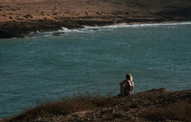cabo_de_la_vela_colombia una chica sentada en unas rocas mirando hacia la playa