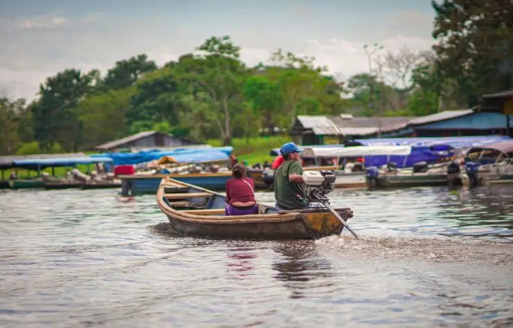 Personas navegando en una canoa con motor en el río Amazonas, en Leticia, rodeados de casas y embarcaciones típicas de la región.