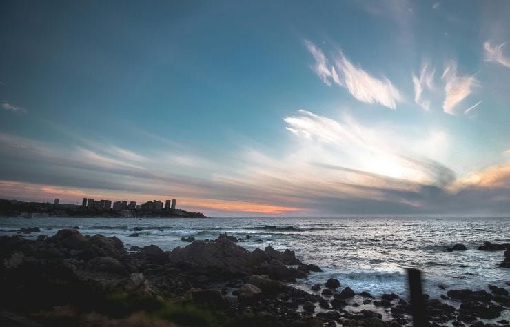 Atardecer en la costa rocosa de Viña del Mar, Chile, con el océano Pacífico y la ciudad al fondo.